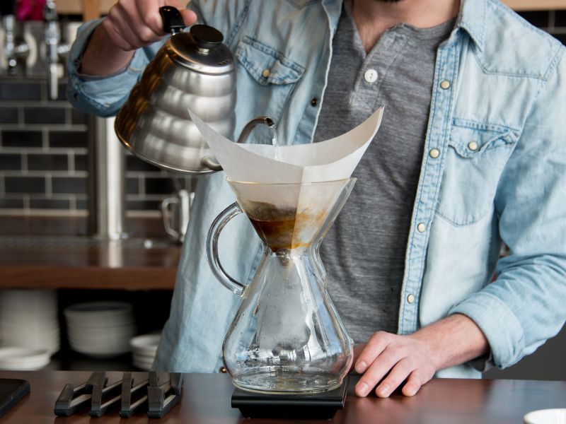 man pouring water from steel gooseneck kettle into chemex brewer