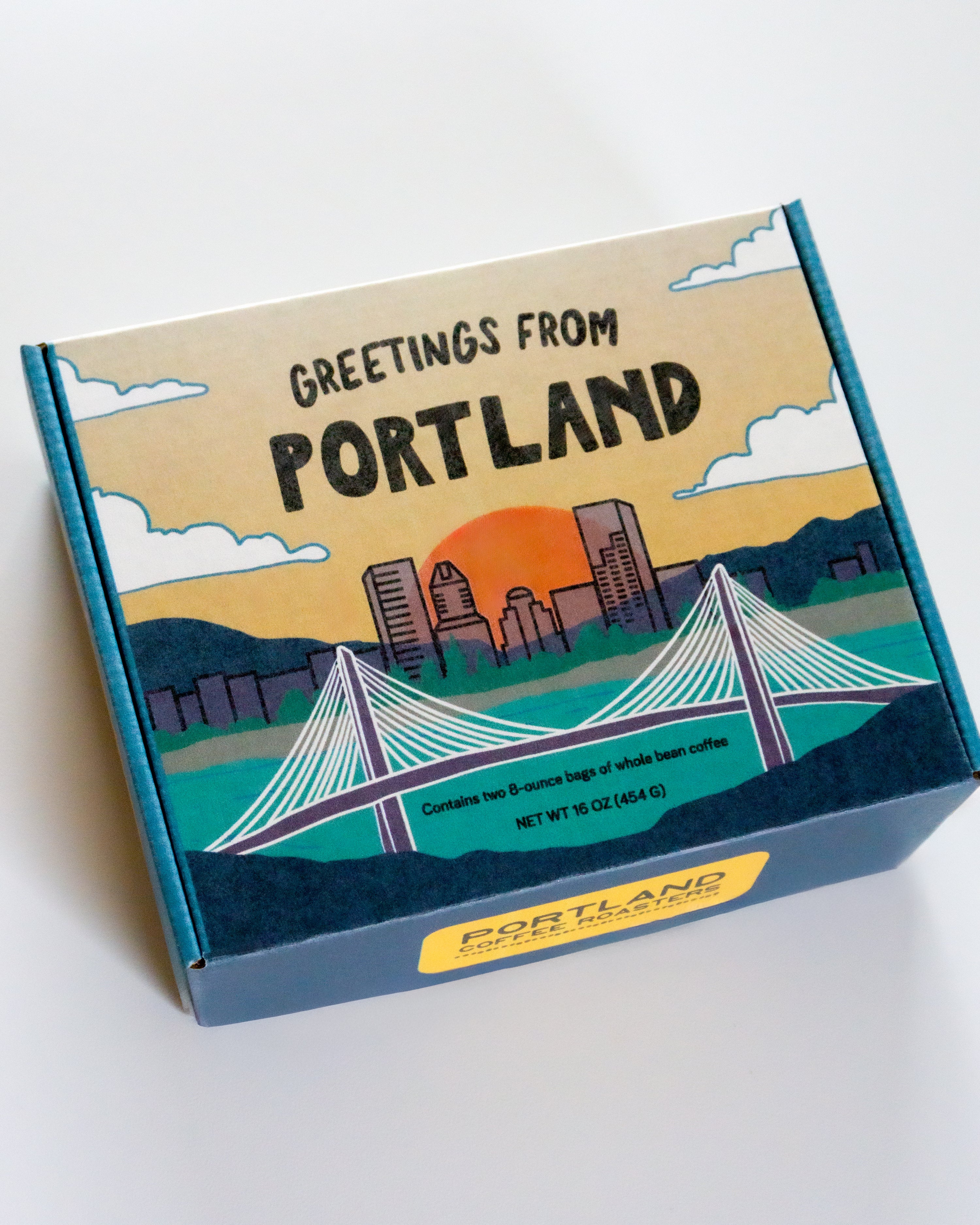 Box of Portland Coffee Roasters coffee, decorated with an illustrated landscape of Portland, Oregon, including the cityscape, bridges, and a sunset. The box reads "Greetings From Portland" across the top.