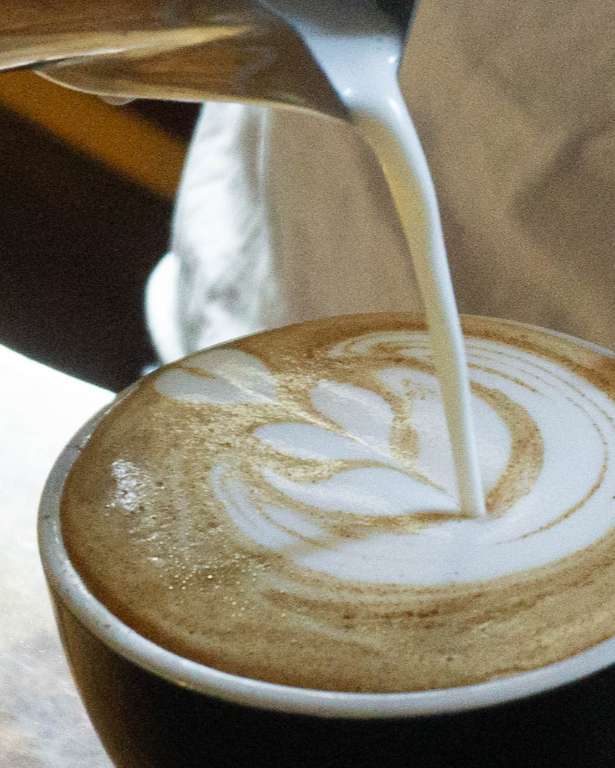 Pouring milk into a coffee cup to create latte art on a wooden surface.